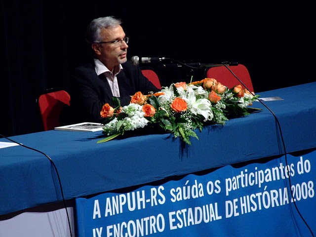 Manoel Salgado sentado em mesa de congresso. Na toalha da mesa: Anpuh saúda os participantes do IX encontro estadual de história 2008 o logo do evento ANPUH