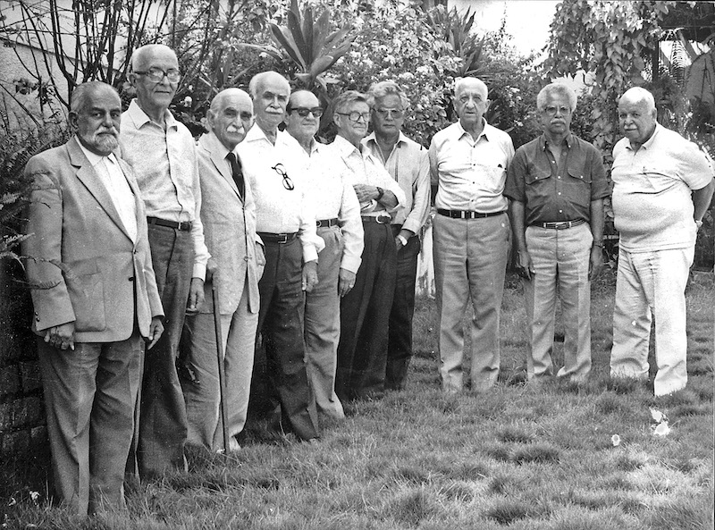 Dez homens já idosos em pé posando para foto com semblante sério