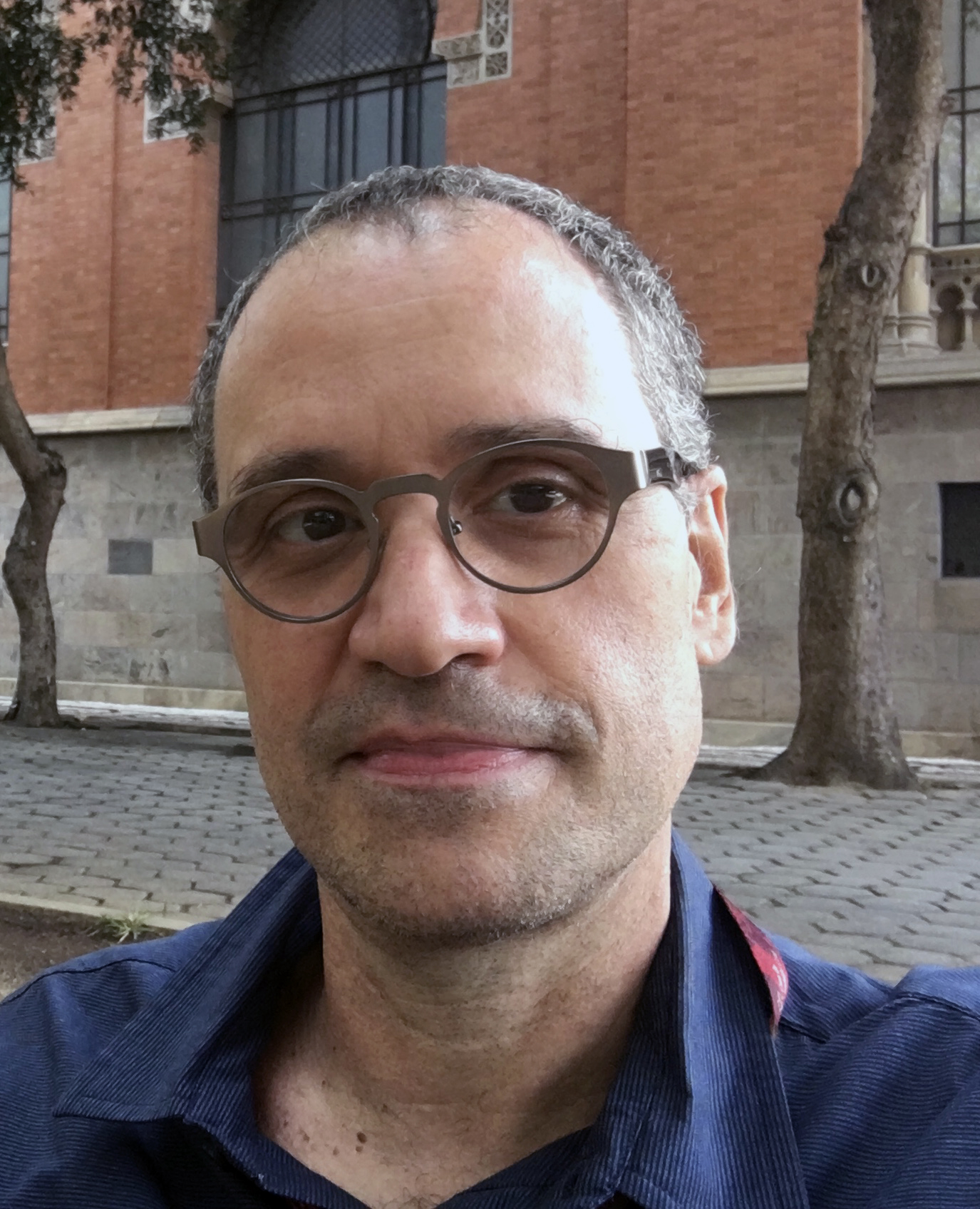 Foto de Renato Gama-Rosa, de óculos, camisa azul e tendo ao fundo praça ao lado do Castelo da Fiocruz