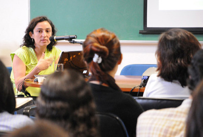 A pesquisadora Kátia Lerner, sentada em frente ao microfone, diante da plateia.